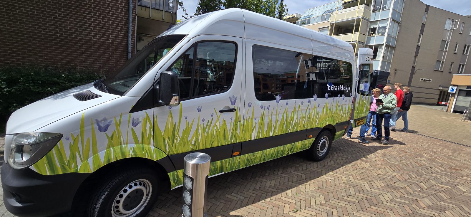 De rolstoelbus van 't Grasklokje, vooraanzicht, beschilderd met gras en paarse tulpen